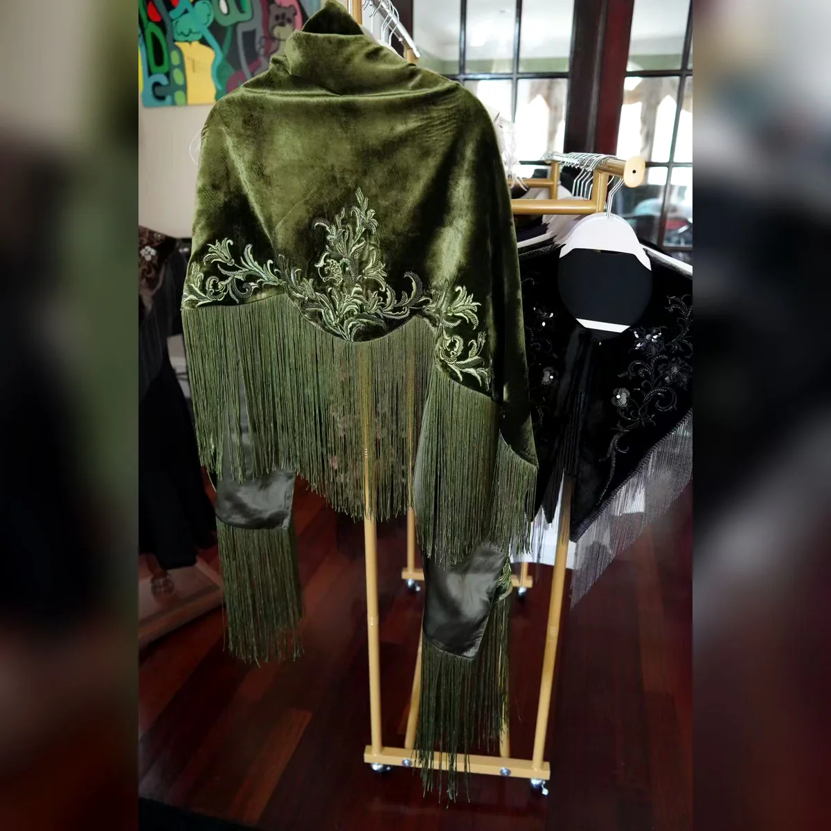 Olive velvet embroidered fringe shawl on a garment rack